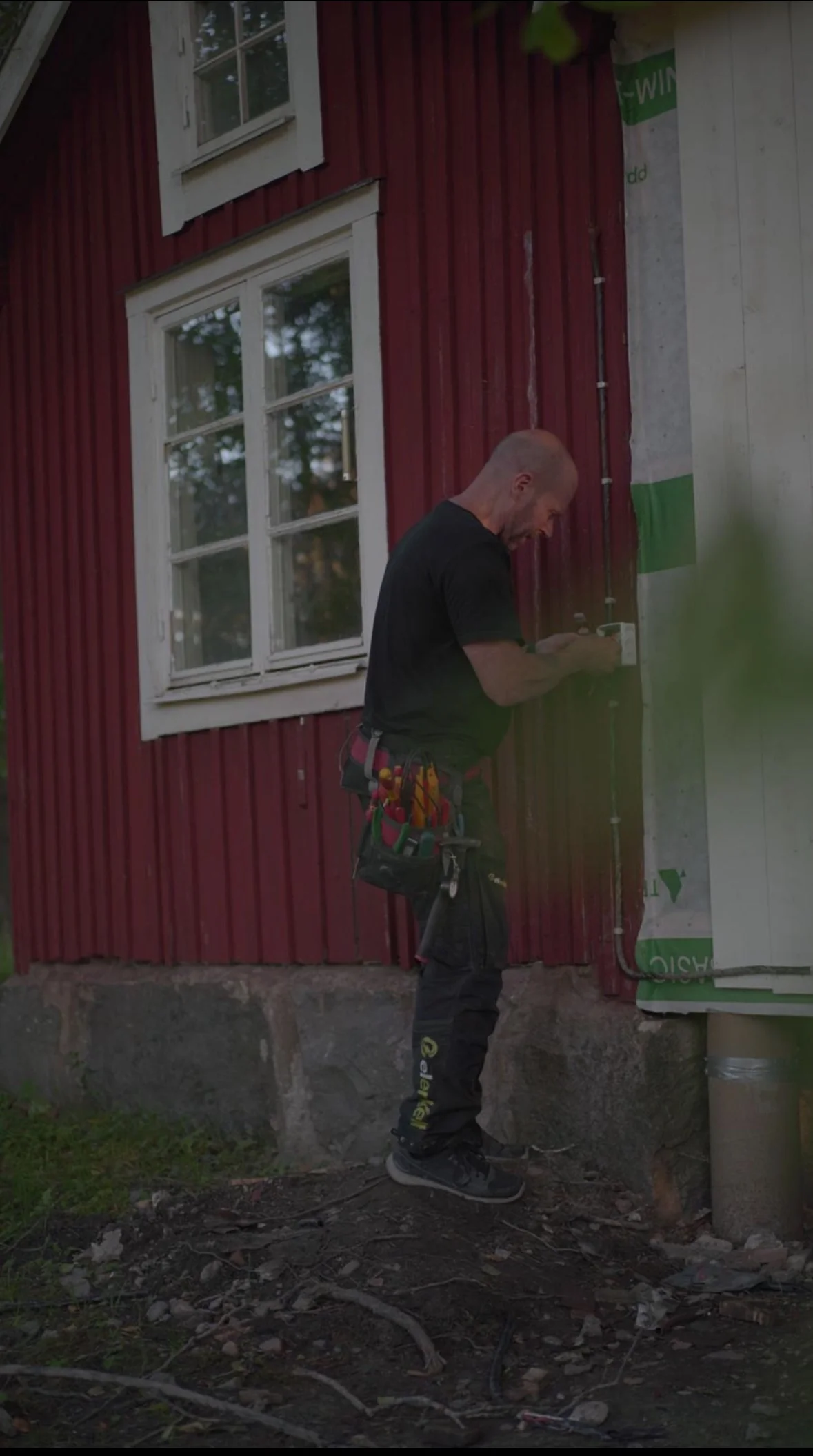 Elenkelt elektriker installerar el på röd svensk stuga